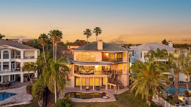 back of property at dusk featuring a chimney, an outdoor pool, a jacuzzi, and a patio area