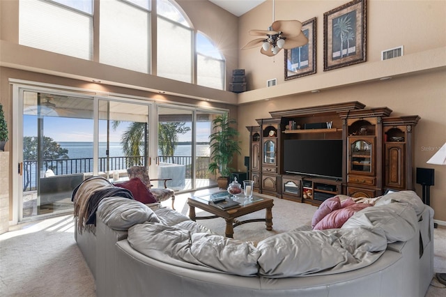 living room featuring a high ceiling, carpet floors, ceiling fan, and visible vents