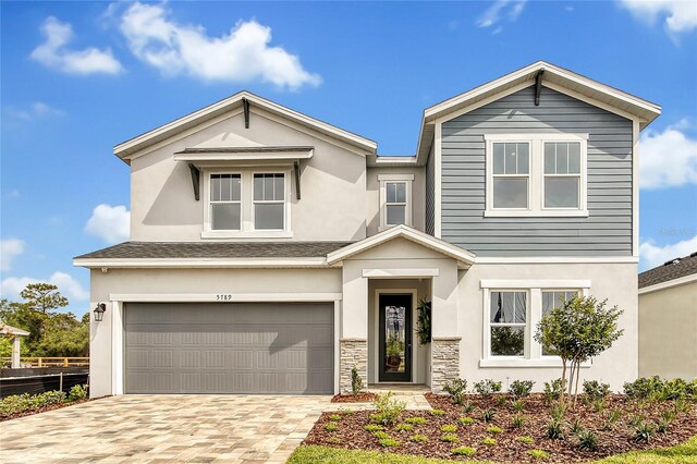 view of front of property featuring an attached garage, stone siding, decorative driveway, and stucco siding