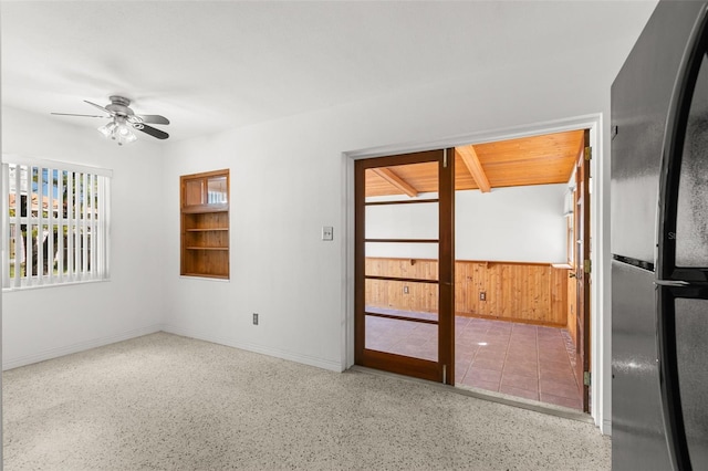 empty room featuring a wainscoted wall, ceiling fan, light speckled floor, and wood walls