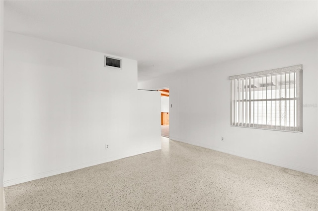 empty room with speckled floor, visible vents, and baseboards