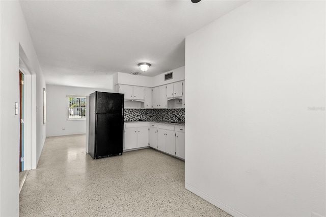 kitchen with tasteful backsplash, freestanding refrigerator, white cabinetry, and visible vents