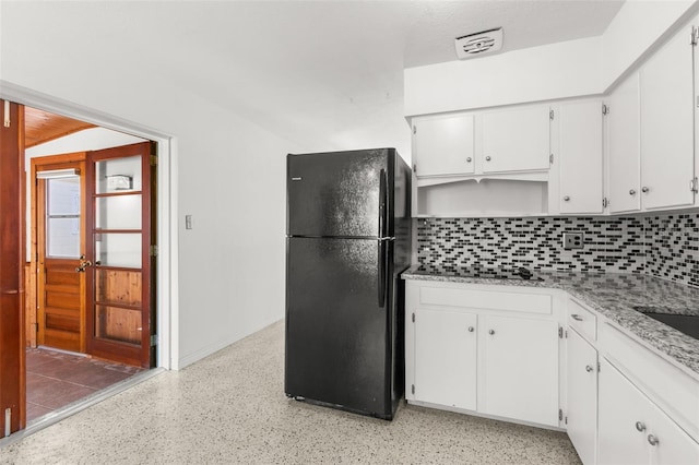 kitchen with light speckled floor, light stone counters, white cabinets, freestanding refrigerator, and tasteful backsplash