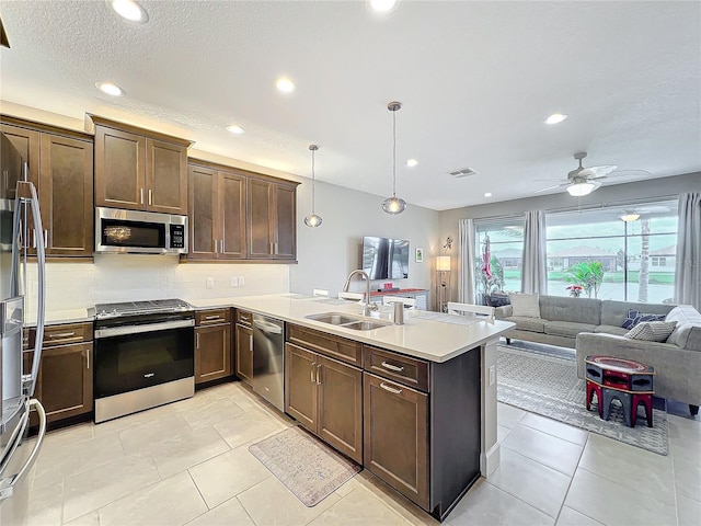 kitchen with light countertops, stainless steel appliances, open floor plan, a sink, and decorative light fixtures