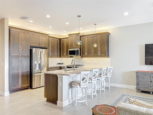 kitchen featuring a kitchen breakfast bar, appliances with stainless steel finishes, light countertops, decorative backsplash, and decorative light fixtures