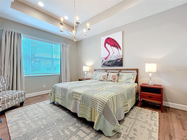 bedroom featuring wood finished floors, baseboards, an inviting chandelier, and a tray ceiling