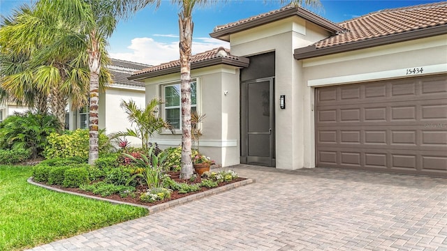 view of front of home with stucco siding, a tile roof, an attached garage, and decorative driveway