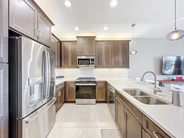 kitchen featuring tasteful backsplash, hanging light fixtures, a sink, stainless steel appliances, and light countertops