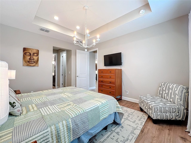 bedroom featuring recessed lighting, a tray ceiling, wood finished floors, baseboards, and a notable chandelier