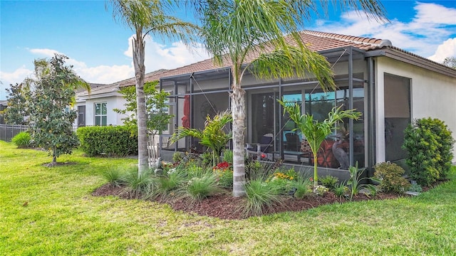 back of property featuring a lawn, a tiled roof, a sunroom, and stucco siding