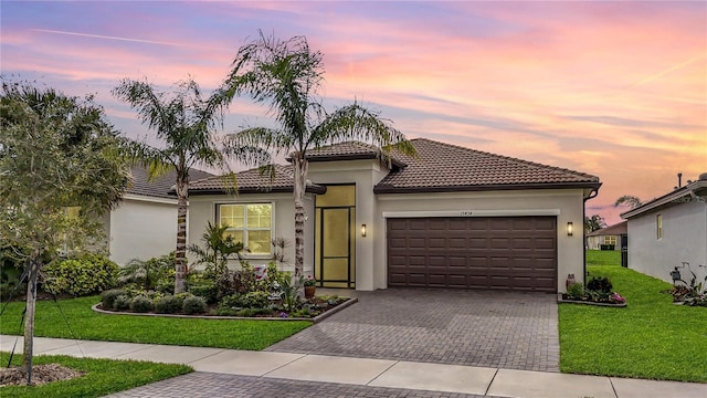 mediterranean / spanish home featuring decorative driveway, a front lawn, a tiled roof, a garage, and stucco siding