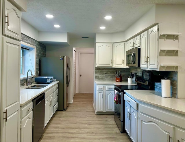 kitchen with stainless steel appliances, light wood-style flooring, a sink, and white cabinetry