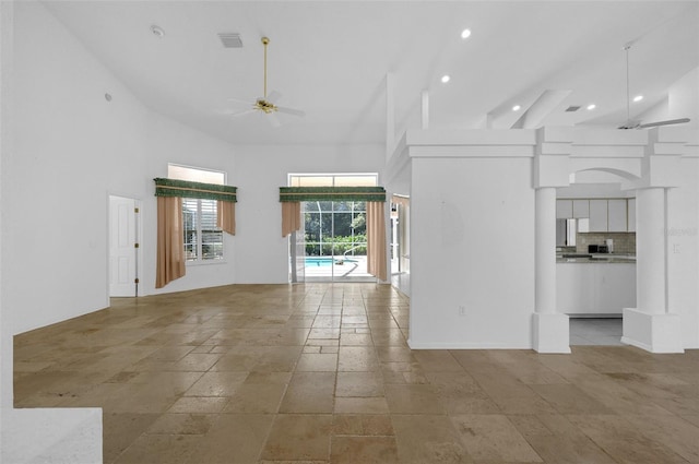 unfurnished living room with visible vents, ceiling fan, a towering ceiling, and stone tile floors