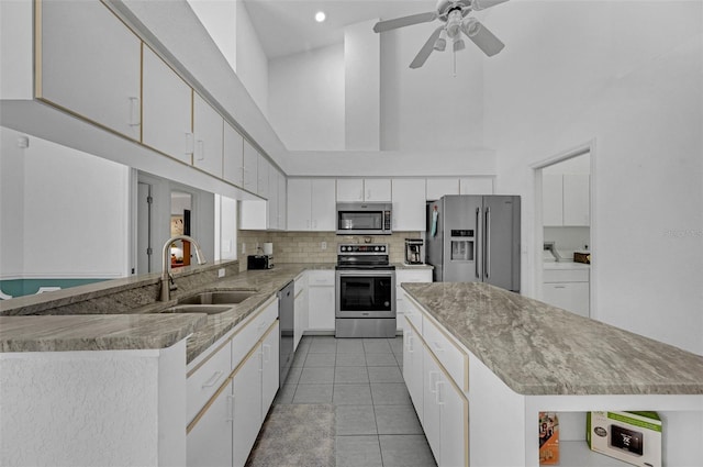 kitchen with stainless steel appliances, a high ceiling, a sink, and white cabinetry