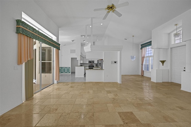 unfurnished living room with high vaulted ceiling, stone tile flooring, and ceiling fan with notable chandelier