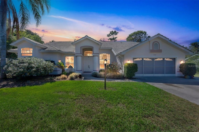 single story home featuring a garage, a lawn, driveway, and stucco siding