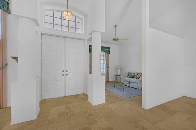 foyer featuring stone finish floor, a towering ceiling, and ceiling fan with notable chandelier