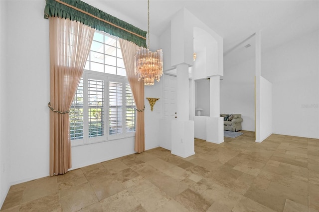 interior space featuring stone finish flooring, a healthy amount of sunlight, a high ceiling, and an inviting chandelier