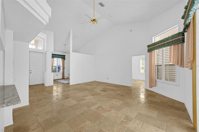 unfurnished living room with high vaulted ceiling, a ceiling fan, visible vents, and stone tile flooring