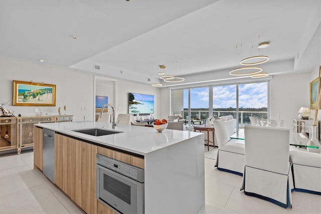 kitchen featuring sink, appliances with stainless steel finishes, an island with sink, decorative light fixtures, and a raised ceiling