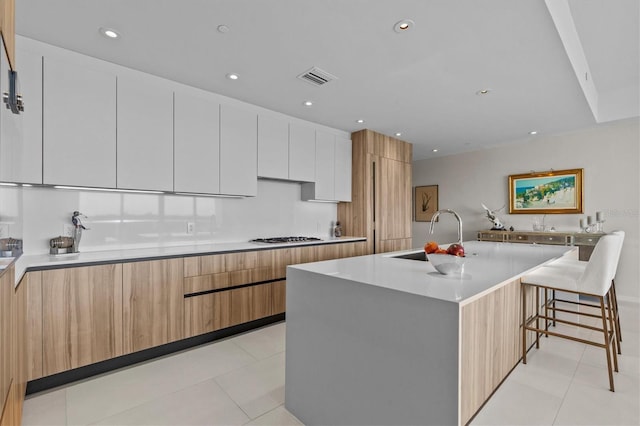 kitchen featuring sink, a breakfast bar area, white cabinets, light tile patterned floors, and a spacious island