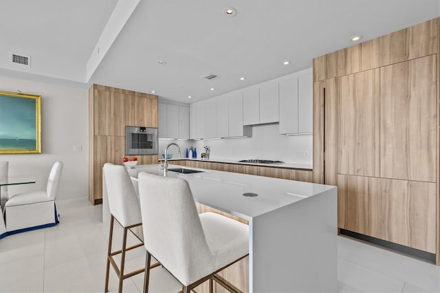 kitchen with a kitchen bar, sink, white cabinetry, appliances with stainless steel finishes, and a large island