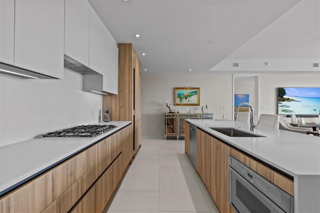 kitchen featuring sink, light tile patterned floors, white cabinets, stainless steel appliances, and wall chimney range hood