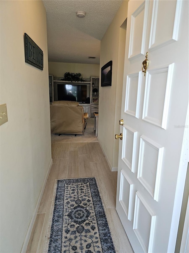 hallway featuring light wood-type flooring and a textured ceiling