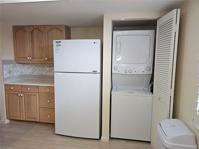 laundry room featuring stacked washing maching and dryer and light hardwood / wood-style floors