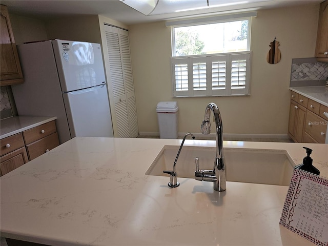 kitchen featuring light stone countertops, white fridge, and backsplash