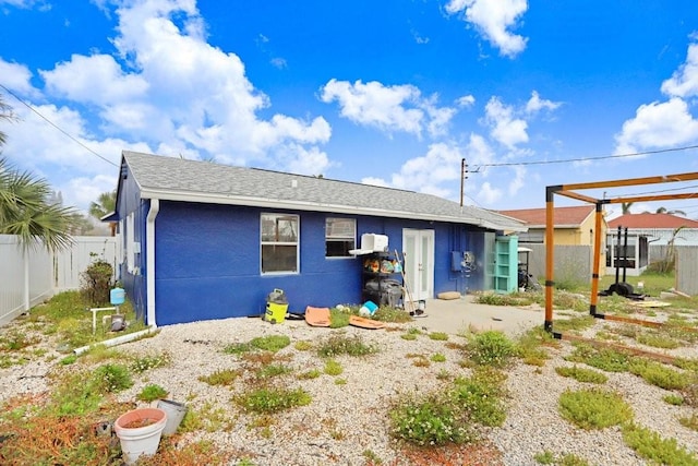 rear view of house featuring roof with shingles, fence private yard, and stucco siding