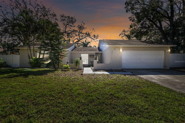 view of front facade with a yard, stucco siding, fence, a garage, and driveway