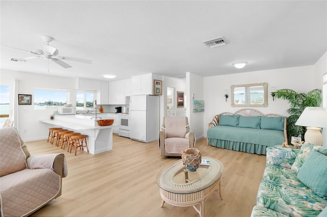 living room with baseboards, visible vents, ceiling fan, and light wood finished floors