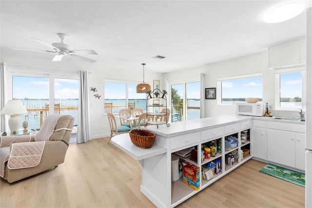 kitchen featuring white microwave, a water view, visible vents, white cabinetry, and light wood finished floors