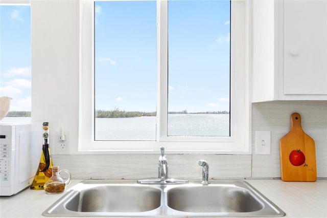 kitchen featuring white microwave, white cabinetry, light countertops, and a sink