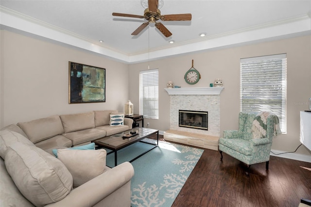 living area featuring a tray ceiling, a glass covered fireplace, crown molding, and wood finished floors