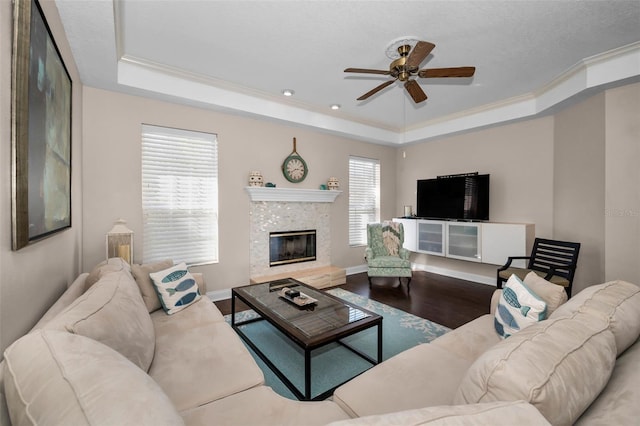 living room with crown molding, a tray ceiling, wood finished floors, and a glass covered fireplace