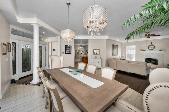 dining space featuring ornate columns, baseboards, a glass covered fireplace, and ceiling fan with notable chandelier