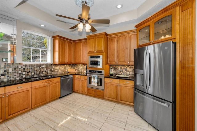 kitchen with glass insert cabinets, appliances with stainless steel finishes, dark stone countertops, brown cabinets, and a sink