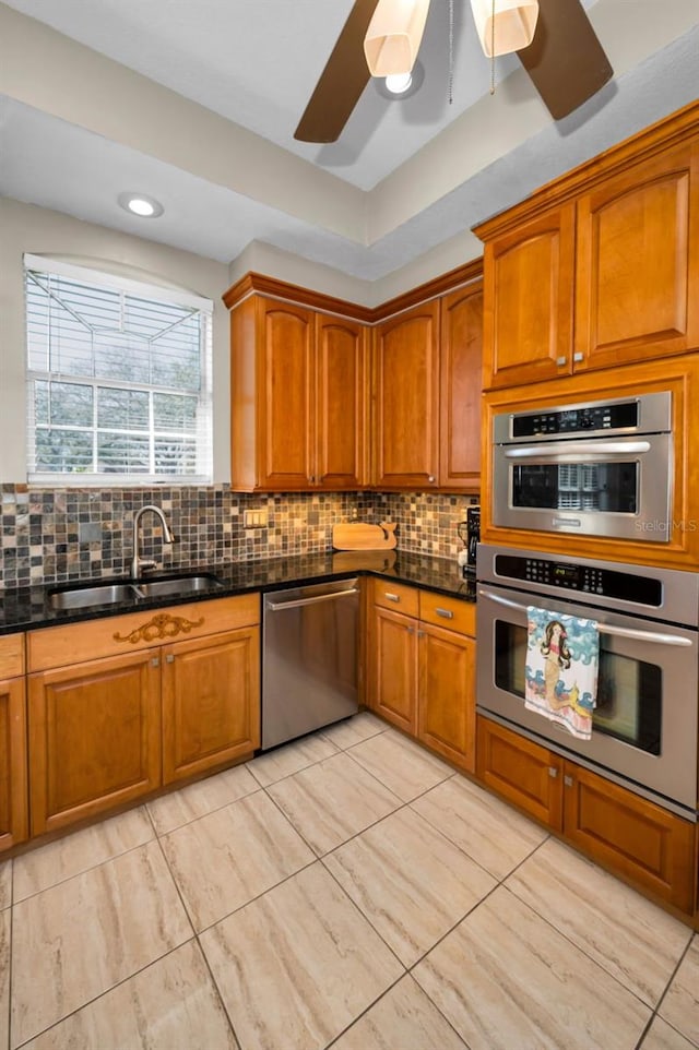 kitchen featuring backsplash, appliances with stainless steel finishes, dark stone counters, and a sink