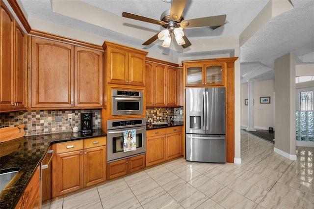 kitchen with stainless steel appliances, brown cabinets, decorative backsplash, dark stone counters, and glass insert cabinets