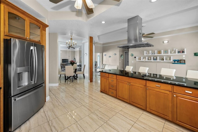 kitchen with ceiling fan with notable chandelier, stainless steel refrigerator with ice dispenser, dark stone countertops, island exhaust hood, and glass insert cabinets