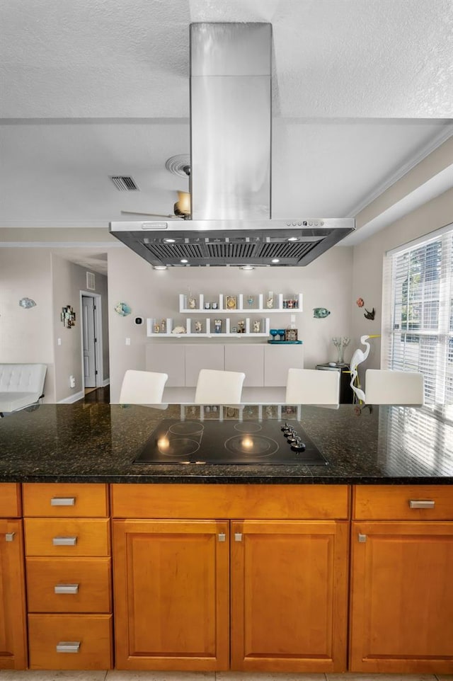 kitchen with visible vents, island range hood, dark stone counters, brown cabinets, and black electric cooktop