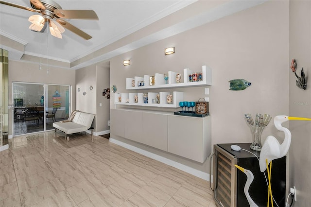 sitting room featuring ceiling fan, baseboards, a raised ceiling, and crown molding