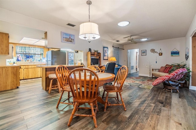 dining space featuring a ceiling fan, a barn door, visible vents, and wood finished floors