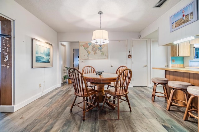 dining room featuring a textured ceiling, wood finished floors, visible vents, and baseboards