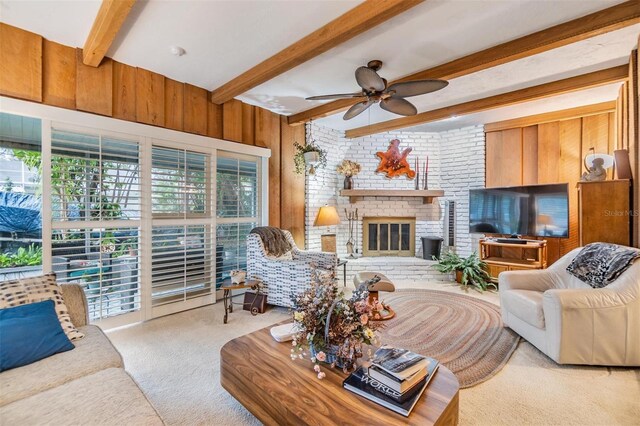 carpeted living area featuring a fireplace, wood walls, beamed ceiling, and ceiling fan