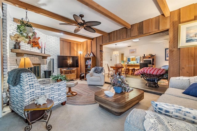 living area with a brick fireplace, beamed ceiling, wooden walls, and ceiling fan