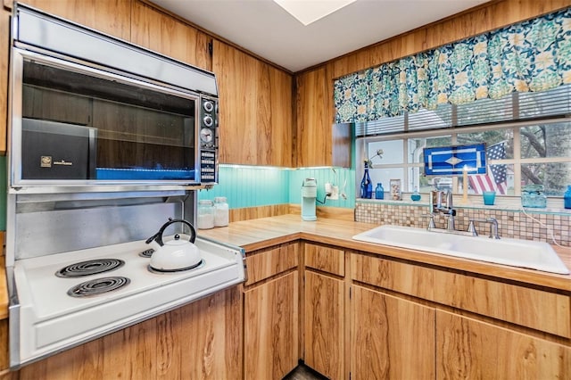 kitchen with brown cabinets, cooktop, light countertops, and a sink