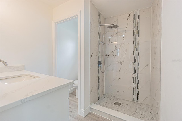 bathroom with tiled shower, vanity, toilet, and wood-type flooring